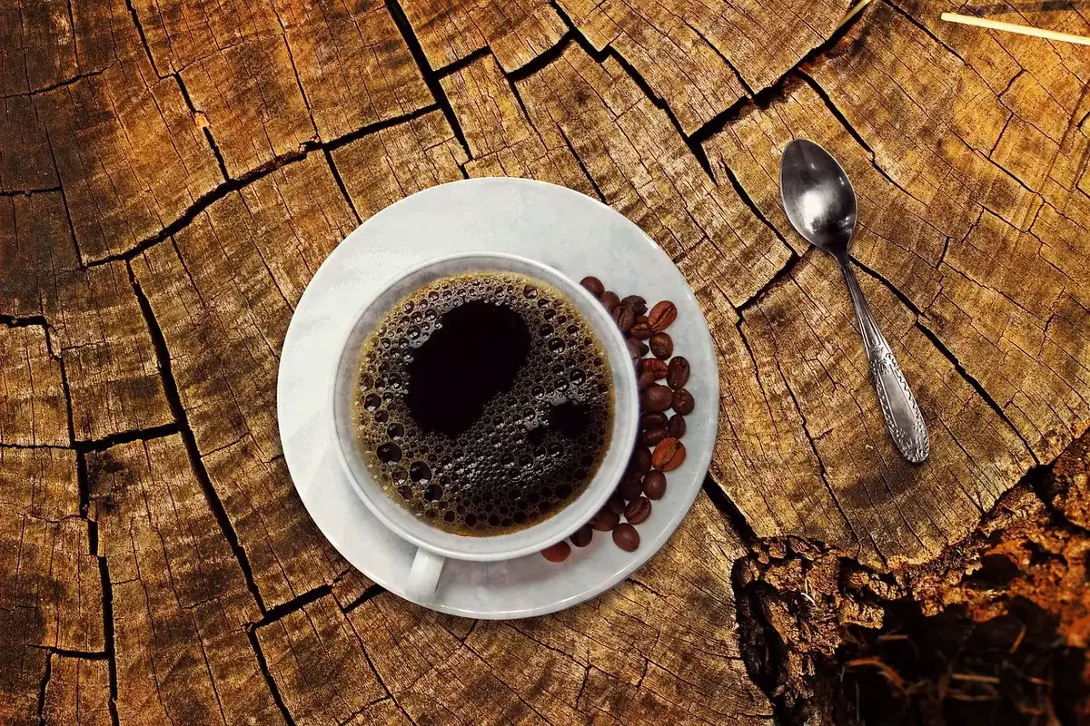 Xícara de café preto com grãos de café no pires, sobre tronco de madeira