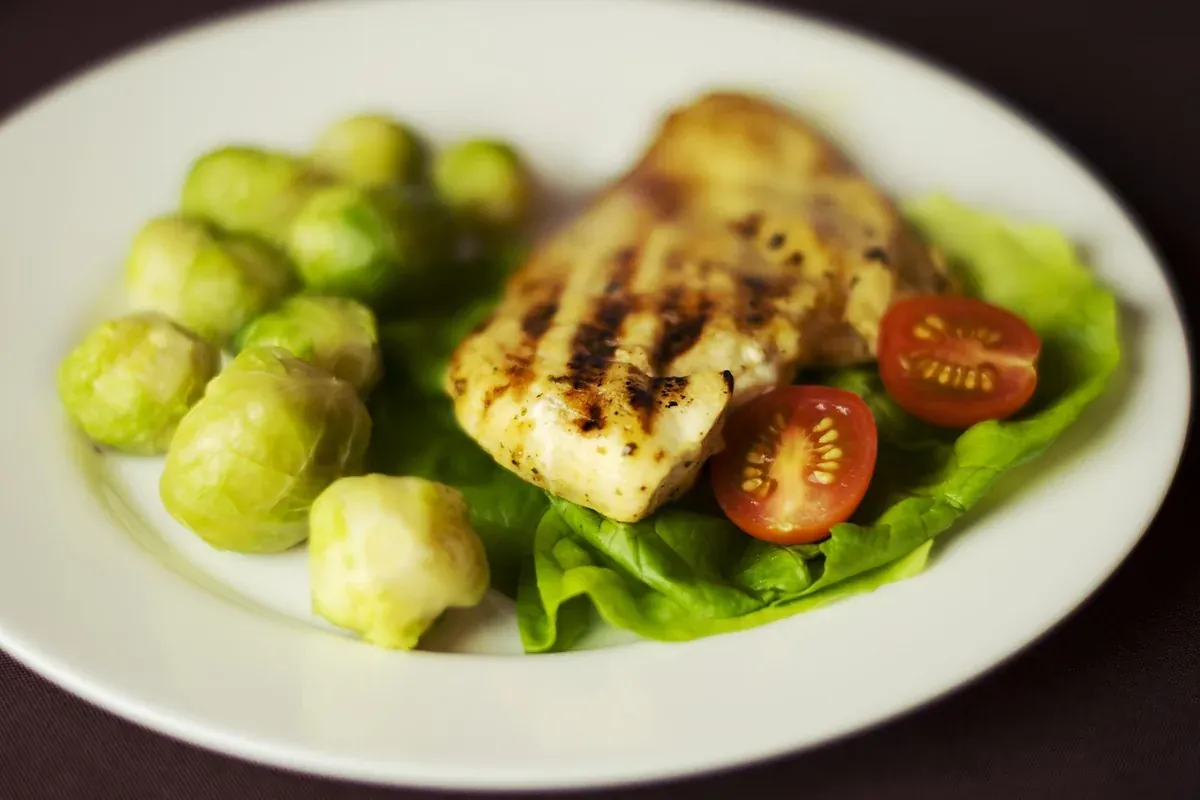 Porção pequena de filé de frango grelhado com couve de bruxelas, alface e tomate cereja